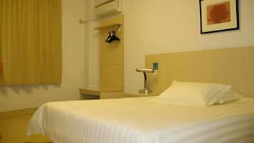 A hotel room with a bed, a nightstand, a wall-mounted lamp, a coat rack, and a window with curtains.