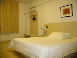 A hotel room with a bed, a nightstand, a wall-mounted lamp, a coat rack, and a window with curtains. - Jinjiang Inn (Shanghai Changzhong Road Subway Station) (Shanghai)