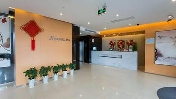 Zona de recepción de un hotel con diseño moderno, que incluye un mostrador de recepción, plantas en macetas y un letrero en la pared.