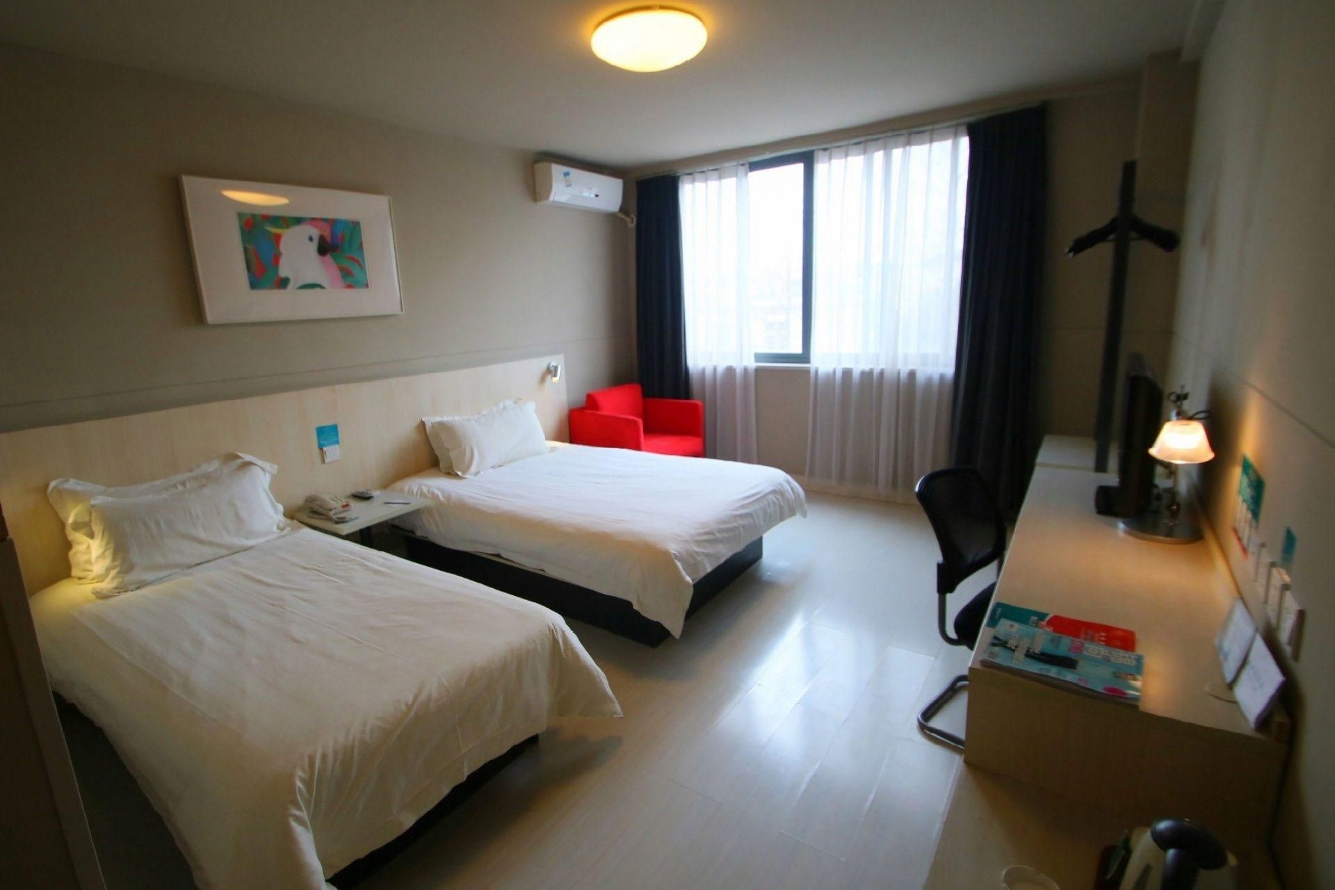 Habitación de hotel con dos camas, un escritorio, una silla, una lámpara y una ventana con cortinas.