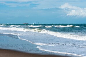 A beach with waves, a cruise ship, and distant structures. - Shoreline view for miles- Oceanfront heated pool (Cape Canaveral)