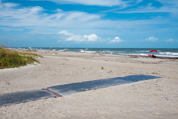 Une plage de sable avec un tapis bleu et un parasol rouge.