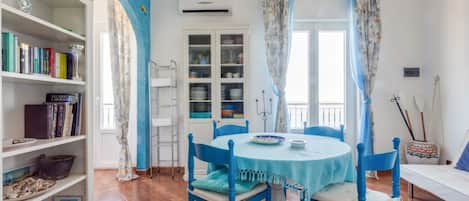 A dining area with a round table, blue chairs, and a bookshelf filled with books and decorative items.