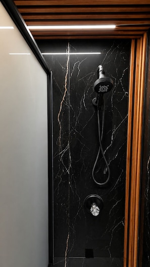 A modern shower with a black marble wall, a wooden panel, and a visible faucet. - Palm's Luxury Suite with Jacuzzi (Aguada)