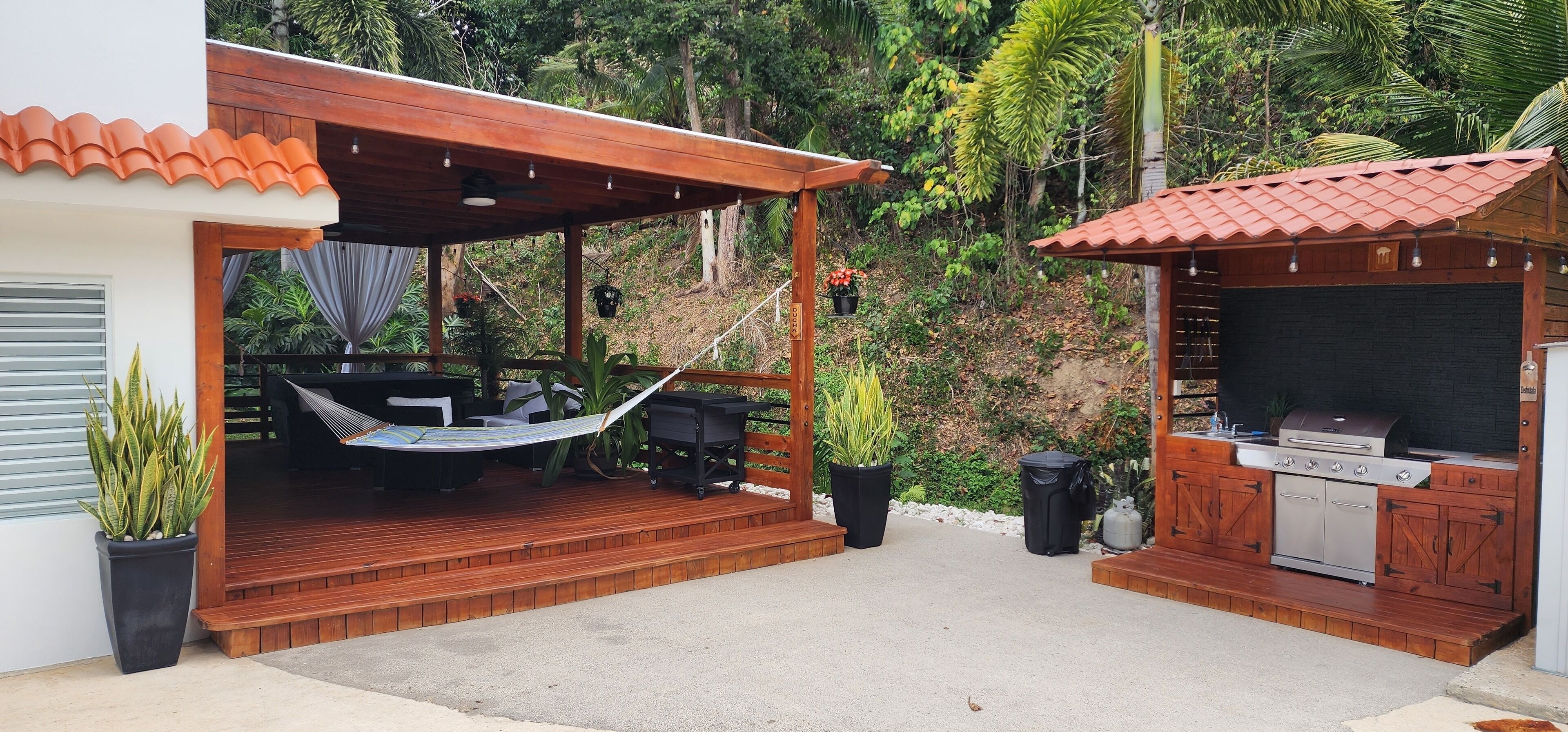 Une terrasse avec un hamac, un barbecue et une plateforme en bois.