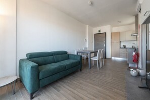 A modern living room with a sofa, dining table, chairs, and a kitchenette.