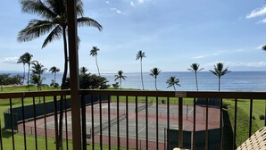 A balcony with a view of a tennis court, palm trees, and the ocean. -  OCEAN FRONT: spacious, remodeled 4th floor condo (Kihei)