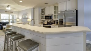 Eine moderne Küche mit weißen Schränken, Edelstahlgeräten, einer großen Kochinsel mit Barhocker und einem Deckenventilator.