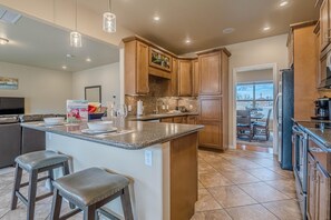 A modern kitchen with wooden cabinets, a granite countertop, and a large island with bar stools. - Sunshine II – Bike Path Access, Close to Town (Fruita)