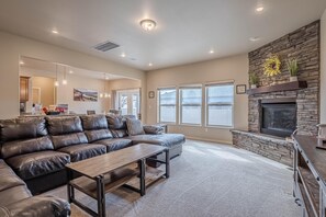 A modern living room with a stone fireplace, leather sectional sofa, and a wooden coffee table. - Sunshine II – Bike Path Access, Close to Town (Fruita)