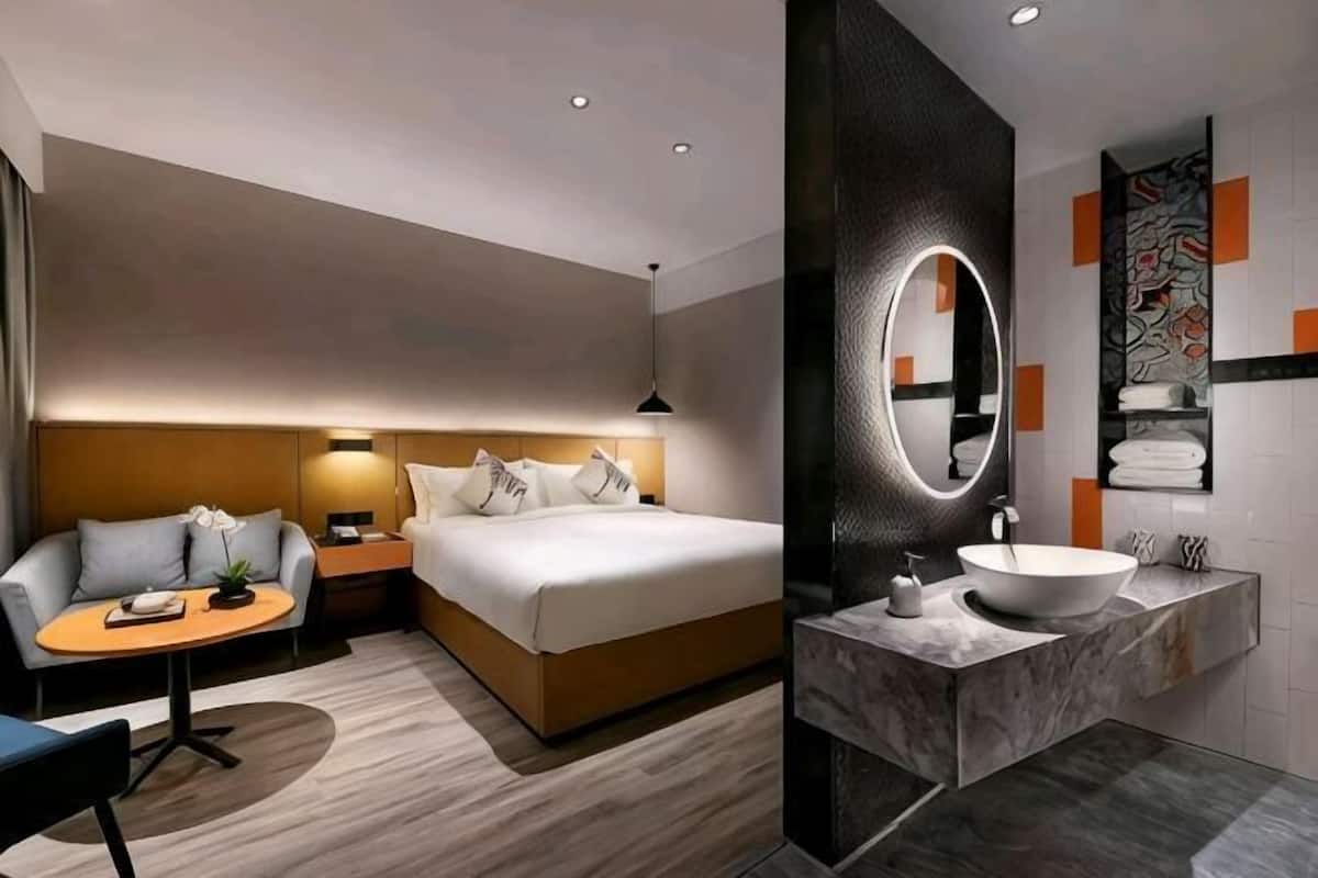 Una habitación de hotel moderna con una cama, una mesita de noche, una lámpara y una mesa redonda con una silla.