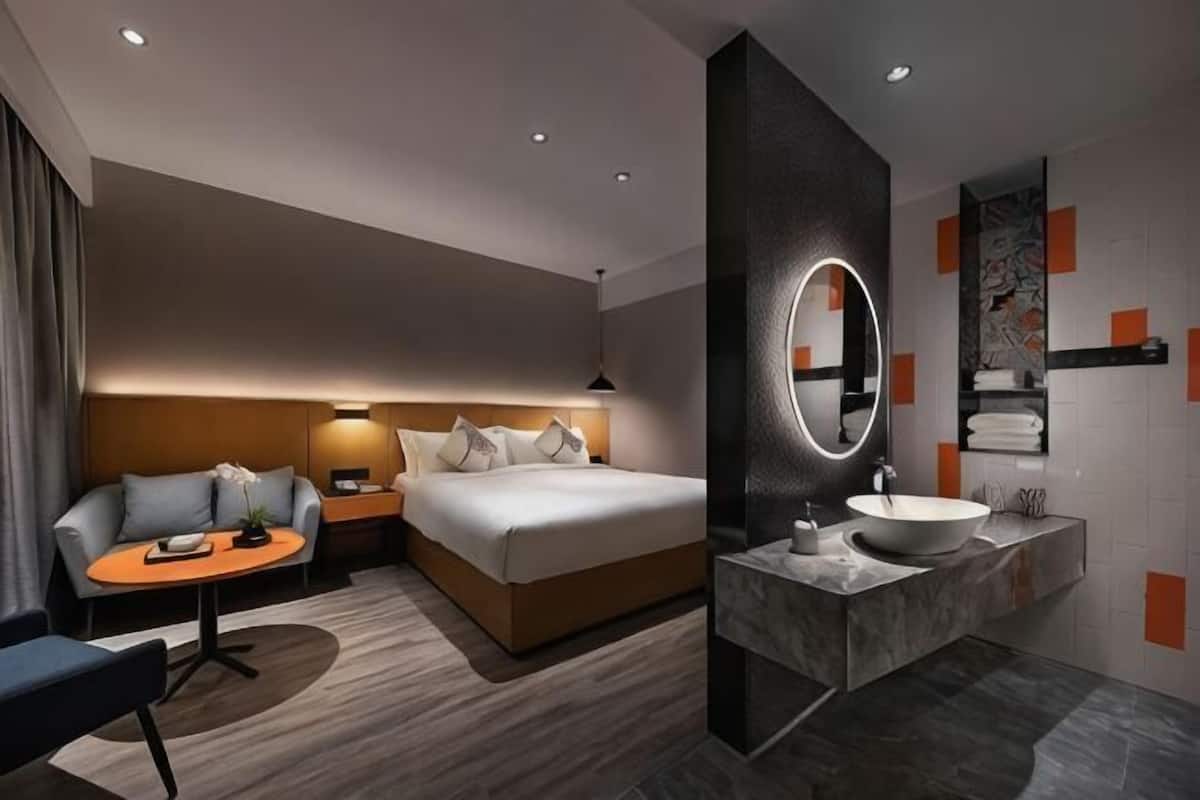 Una habitación de hotel moderna con cama, mesita de noche, lámpara y una mesa redonda con una silla.