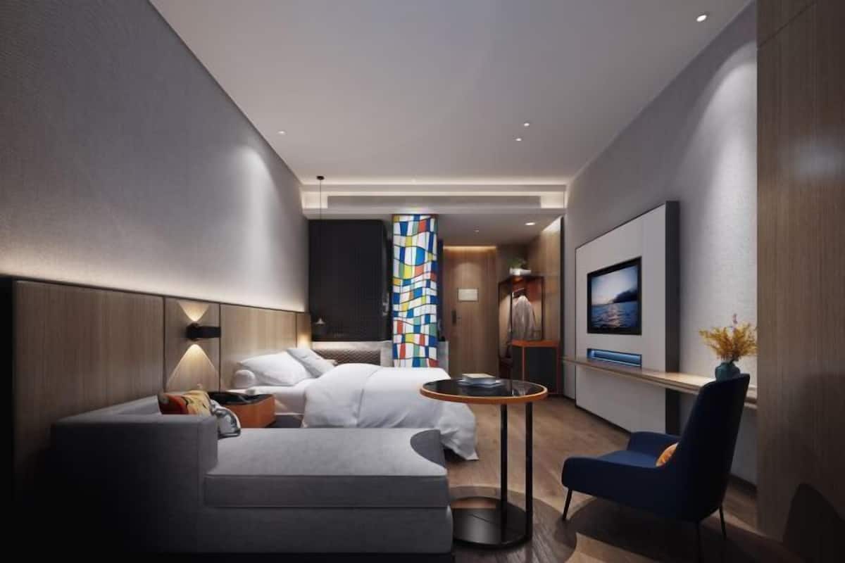 Una habitación de hotel moderna con una cama, un sofá, una mesita y un televisor.