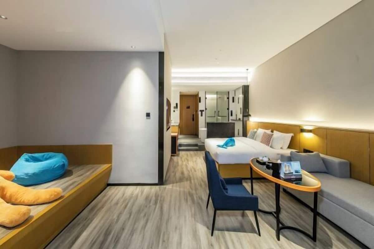 Una habitación de hotel moderna con una cama, una zona de estar con un sillón de saco, una mesita y un sofá.