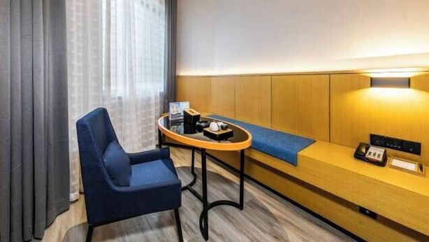 A hotel room with a blue chair, a small round table, a wooden bench, and a wall-mounted lamp. - Sofis POP Hotel (Fuzhou)