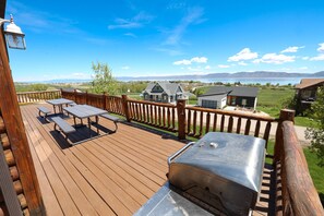 A wooden deck with picnic tables and a barbecue grill, overlooking a lake and distant mountains. - Raspberry Bear Lake Lodge - 6 Bed 3 Bath. Great View Of The Lake! Perfect For Big Families! (Garden City)