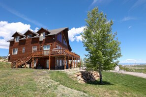 A large wooden house with a balcony, a stone wall, and a tree in the yard. - Raspberry Bear Lake Lodge - 6 Bed 3 Bath. Great View Of The Lake! Perfect For Big Families! (Garden City)