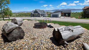 A residential area with houses, a fire pit, and a clear view of mountains in the background. - Raspberry Bear Lake Lodge - 6 Bed 3 Bath. Great View Of The Lake! Perfect For Big Families! (Garden City)
