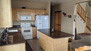 A compact kitchen with wooden cabinets, a stove, a refrigerator, and a granite countertop. - Raspberry Bear Lake Lodge - 6 Bed 3 Bath. Great View Of The Lake! Perfect For Big Families! (Garden City)