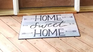 Une porte d’entrée en bois avec un panneau de verre et un paillasson sur lequel est écrit : « Chez soi, on est bien ».