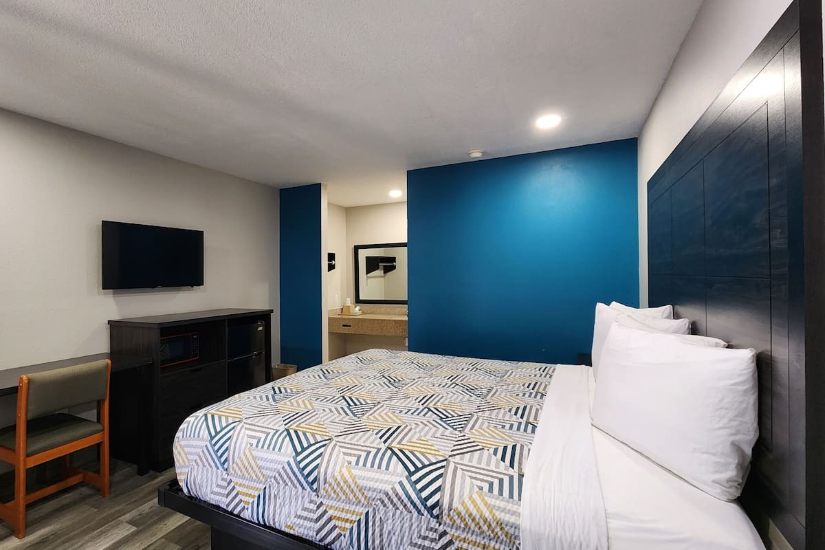 A hotel room with a bed, a desk with a TV, a microwave, and a small cabinet.