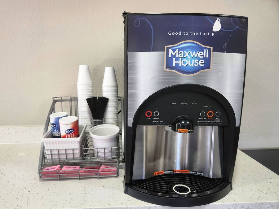 A water dispenser branded 'Maxwell House' with a stainless steel design, a cup holder, and a tray with disposable cups and a coffee cup.