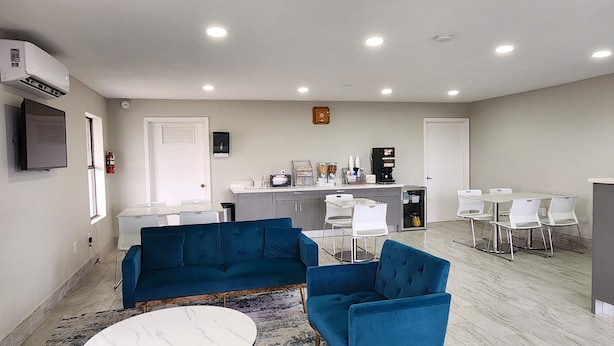 A modern, well-lit room with a sofa, chairs, a coffee machine, and a small kitchen area.