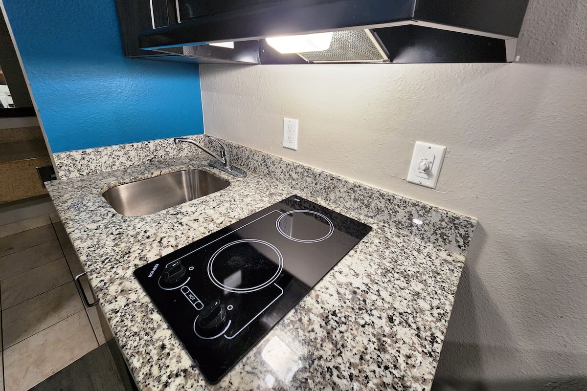 A kitchen with granite countertops, a stainless steel sink, a black induction cooktop, and a wall-mounted oven.