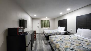 A hotel room with two beds, a desk with a microwave, a TV, and a window with a green curtain.