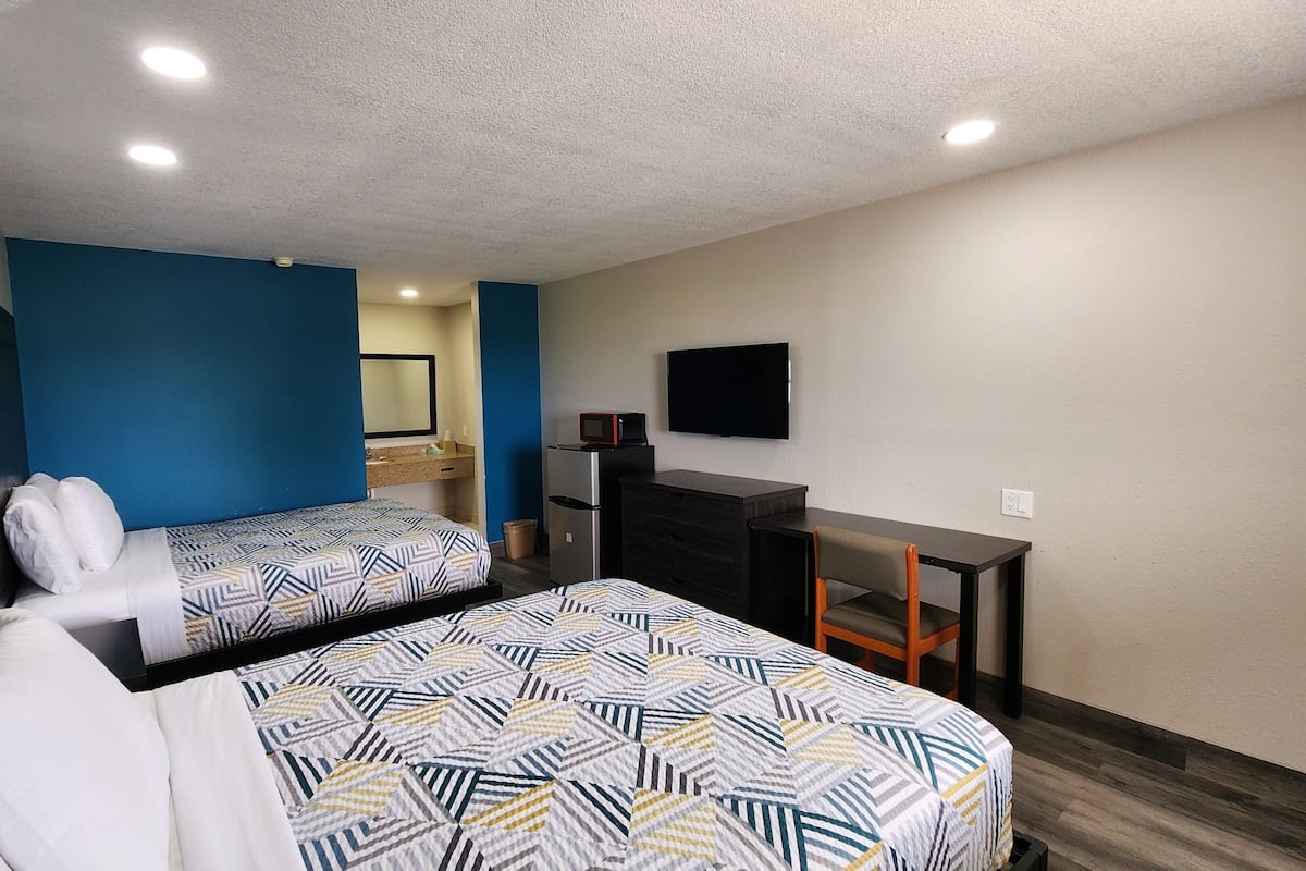 A hotel room with two beds, a desk, a television, and a microwave.
