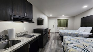 A compact hotel room with a kitchenette, a bed with patterned bedding, and a small sitting area.