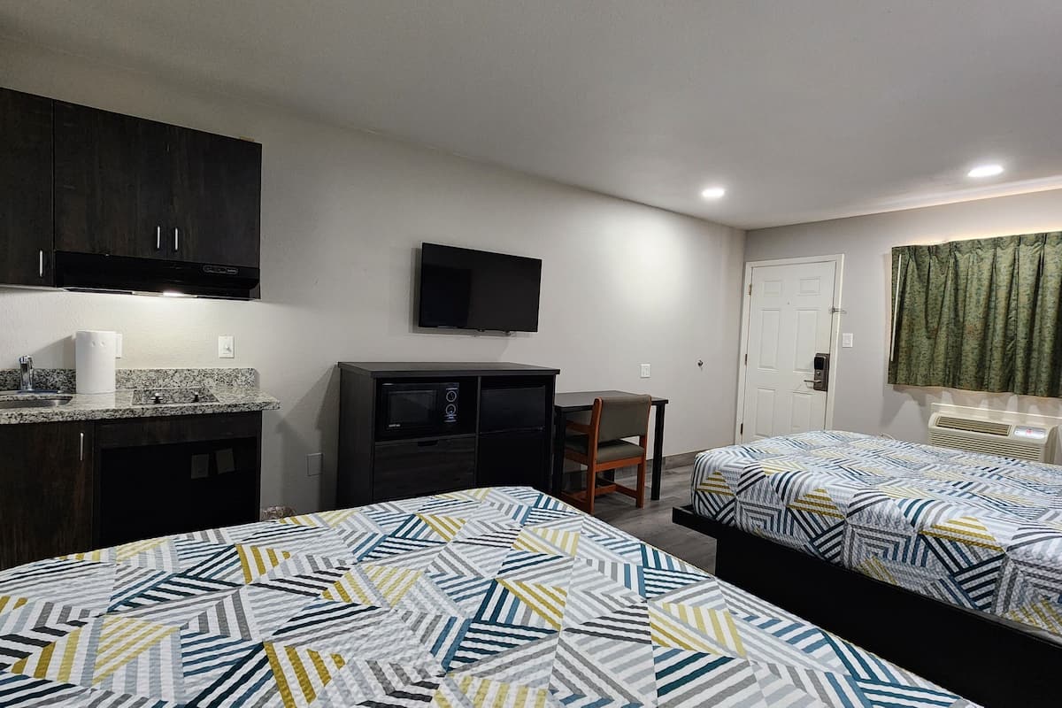 A compact hotel room with two beds, a kitchenette, a TV, and a door with curtains.