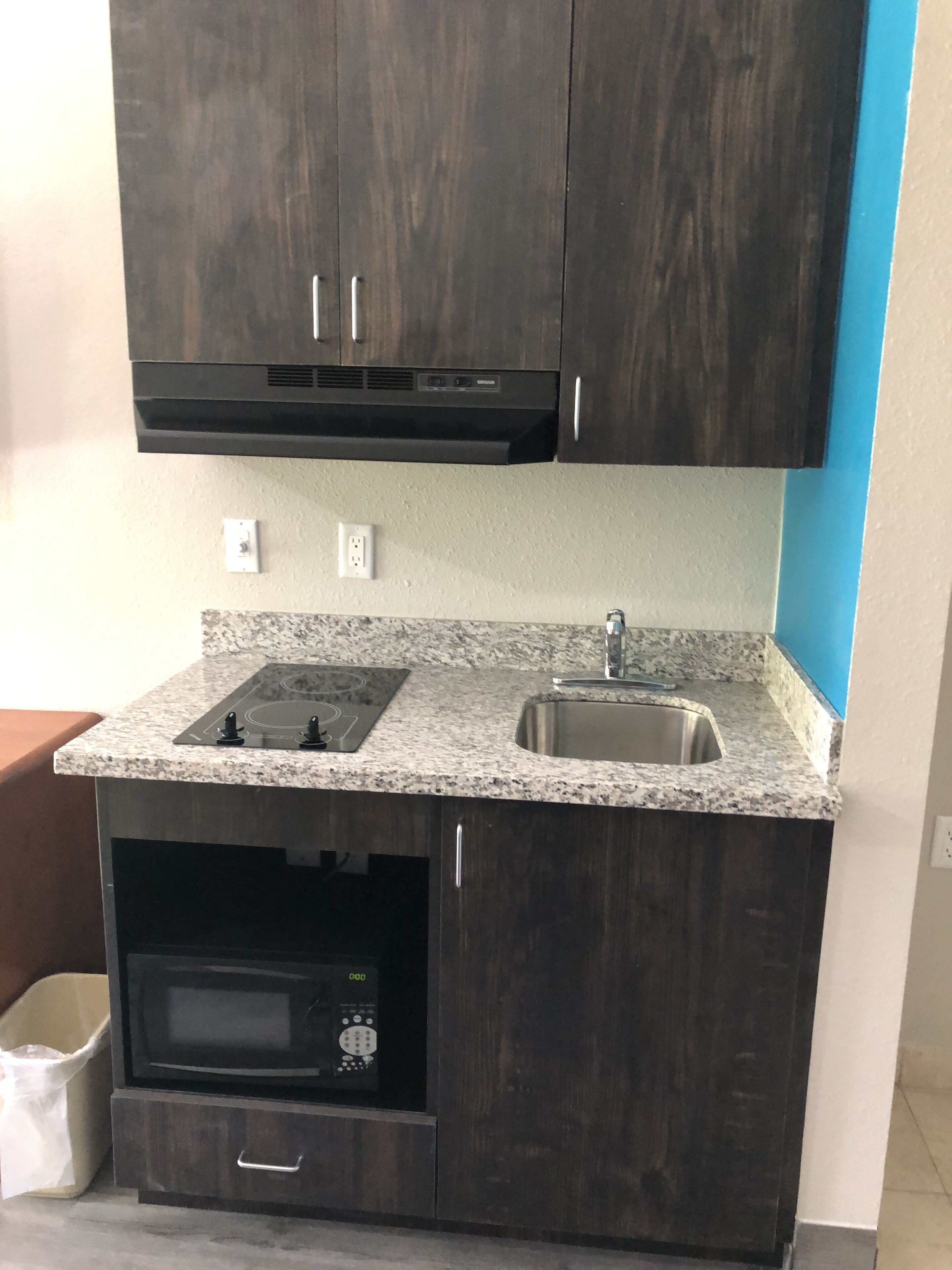 Cocina compacta con alacenas de madera oscura, encimera de granito, horno empotrado y pileta de acero inoxidable.