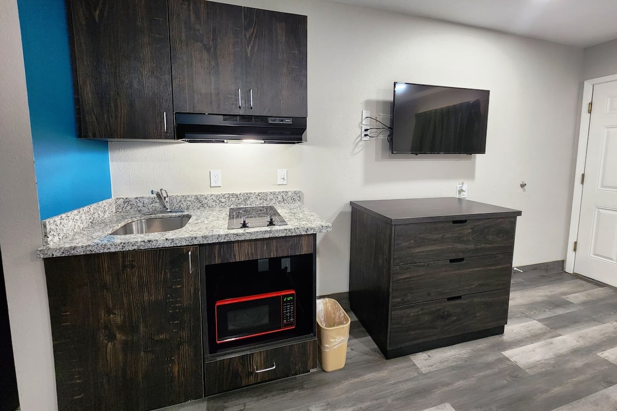 A modern kitchen with dark wood cabinets, a granite countertop, a built-in microwave, and a TV mounted above the counter.
