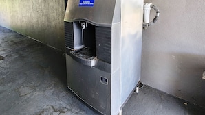 A commercial ice dispenser with a warning label, a water spout, and a metal grate.
