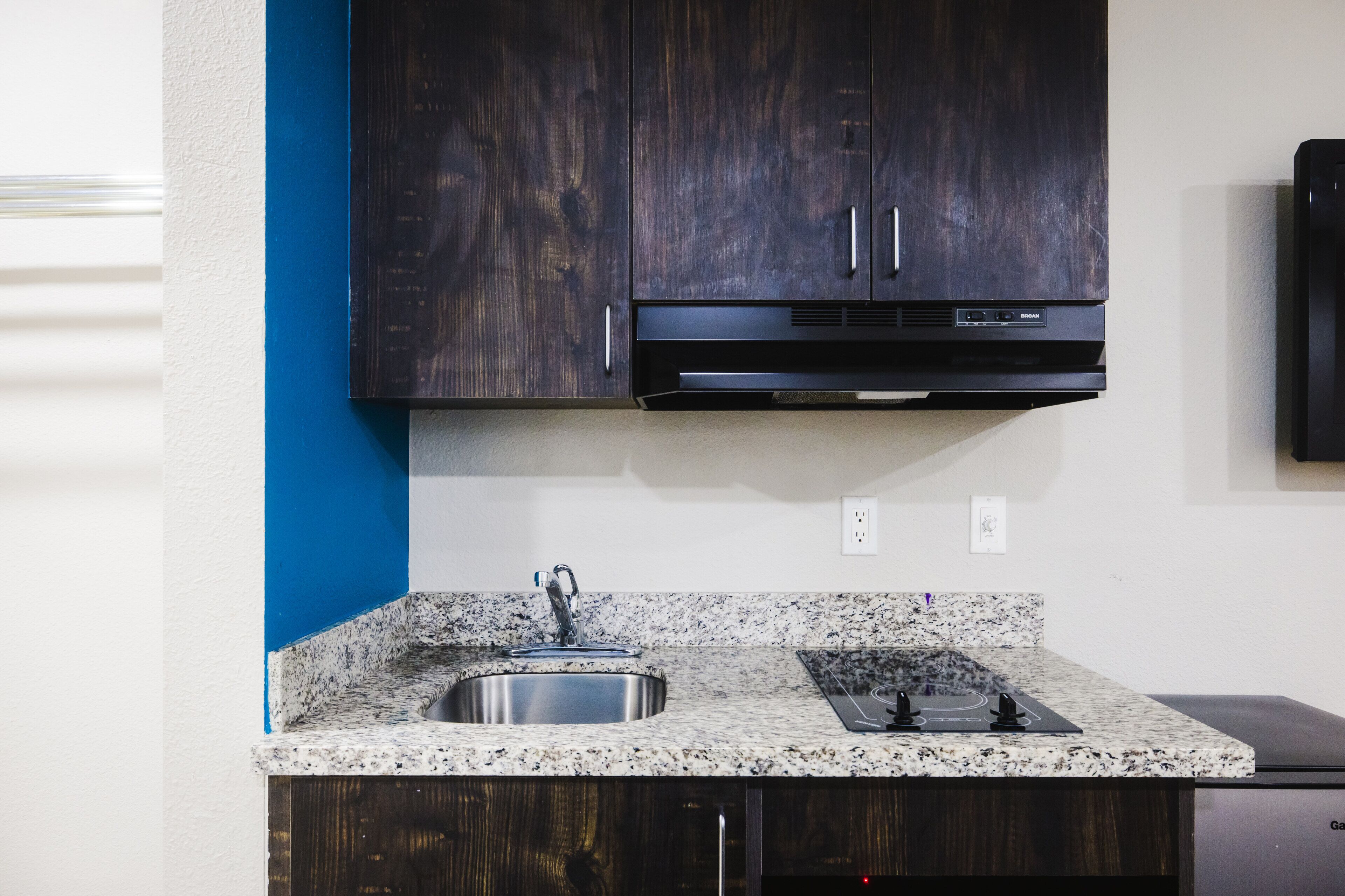 Una cocina con armarios de madera oscura, encimera de granito, pileta de acero inoxidable y extractor de aire negro.