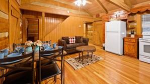 L’intérieur d’une cabane en bois comprend un coin repas, un canapé, un réfrigérateur et des placards en bois.