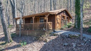 Une cabane en bois dotée d’un porche, entourée d’arbres et bordée d’un chemin de gravier.