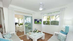 A modern living room with a glass coffee table, white sofas, and a TV mounted on the wall.