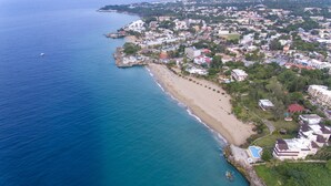 An aerial view of a coastal town with a beach, residential buildings, and a large hotel with a swimming pool.
