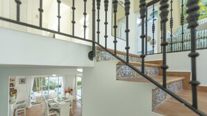 A staircase with a black balustrade leading to a dining area with white furniture and a view of the outdoors.