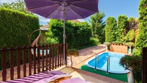 Uma área de piscina privativa com hidromassagem, espreguiçadeiras e um pergolado com guarda-sol.