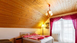 Quarto com teto de madeira, cama com roupa de cama vermelha, mesa de cabeceira, abajur e janela com cortinas vermelhas.