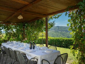 Un espacio de comedor al aire libre techado con una mesa preparada para seis personas, rodeada de sillas y con vistas a un paisaje pintoresco.