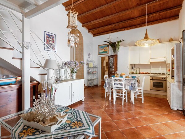 Une cuisine spacieuse avec des meubles blancs, une table à manger pour quatre personnes et un luminaire suspendu.