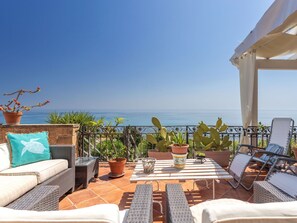 Une terrasse dotée de meubles en osier, de plantes en pot et offrant une vue sur la mer.