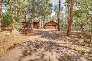 A cabin with a paved driveway leading to a garage, surrounded by tall pine trees. - Deck, Games & Fire Pit: Modern Pine Cabin! (Pine)