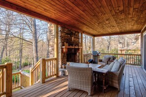 A wooden deck with wicker furniture and a stone fireplace.