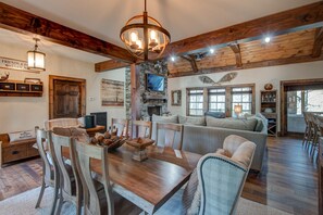 Un intérieur rustique avec une table à manger en bois, des chaises, une cheminée en pierre et un coin salon confortable.