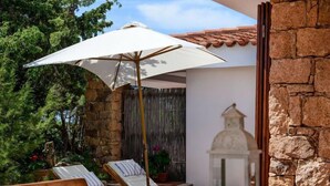 Une terrasse avec des fauteuils de jardin en bois, un parasol blanc et un mur en pierre.